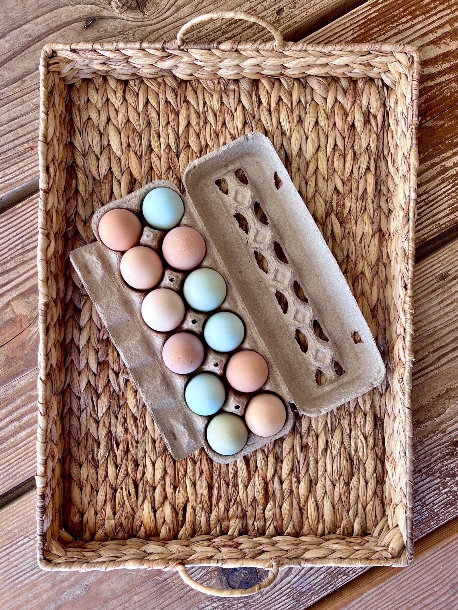 farm-fresh eggs, pastured eggs, colored eggs in carton sitting on woven tray.